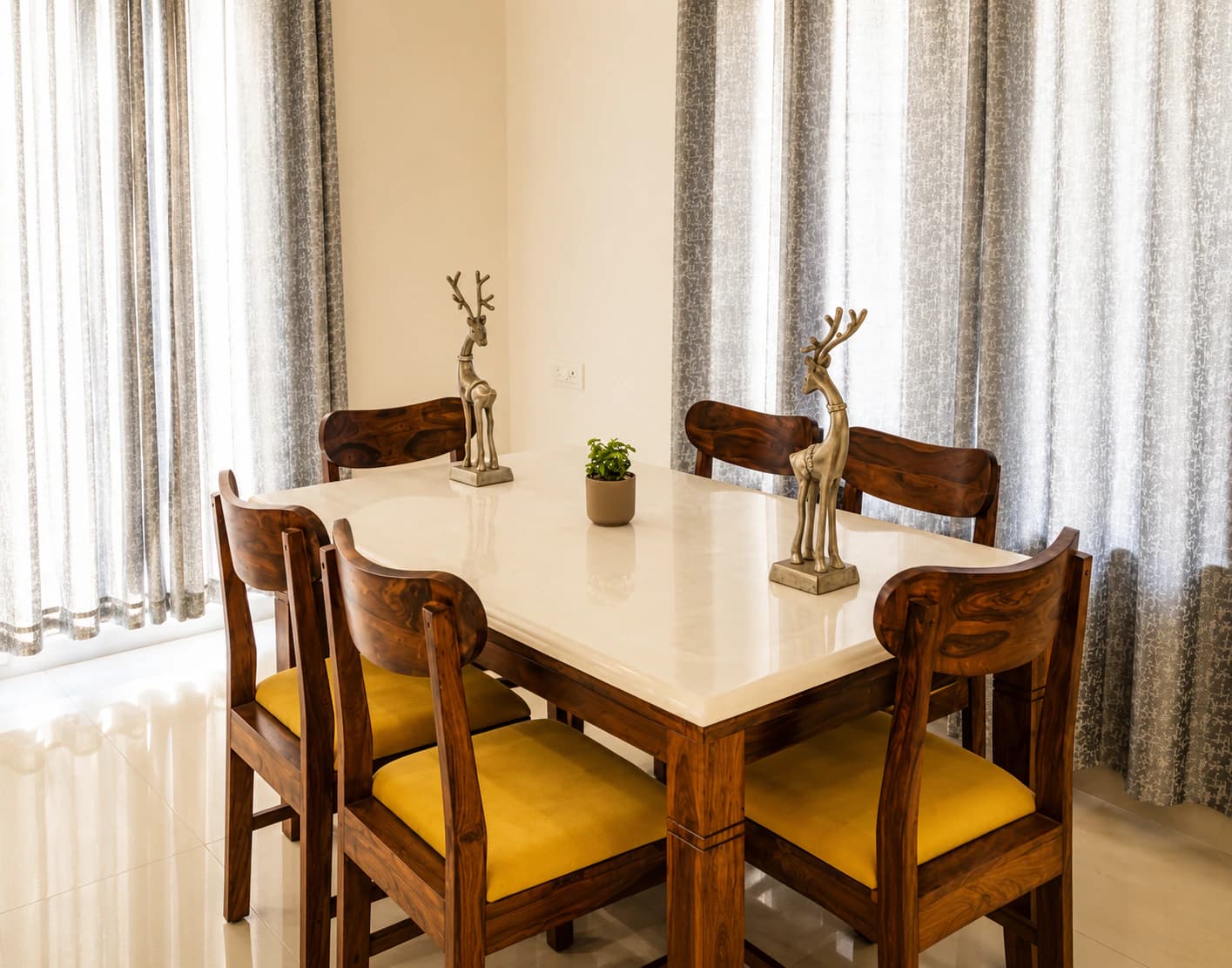 Six-seat wooden dining table with a stone top, cushioned chairs and sheer curtained windows